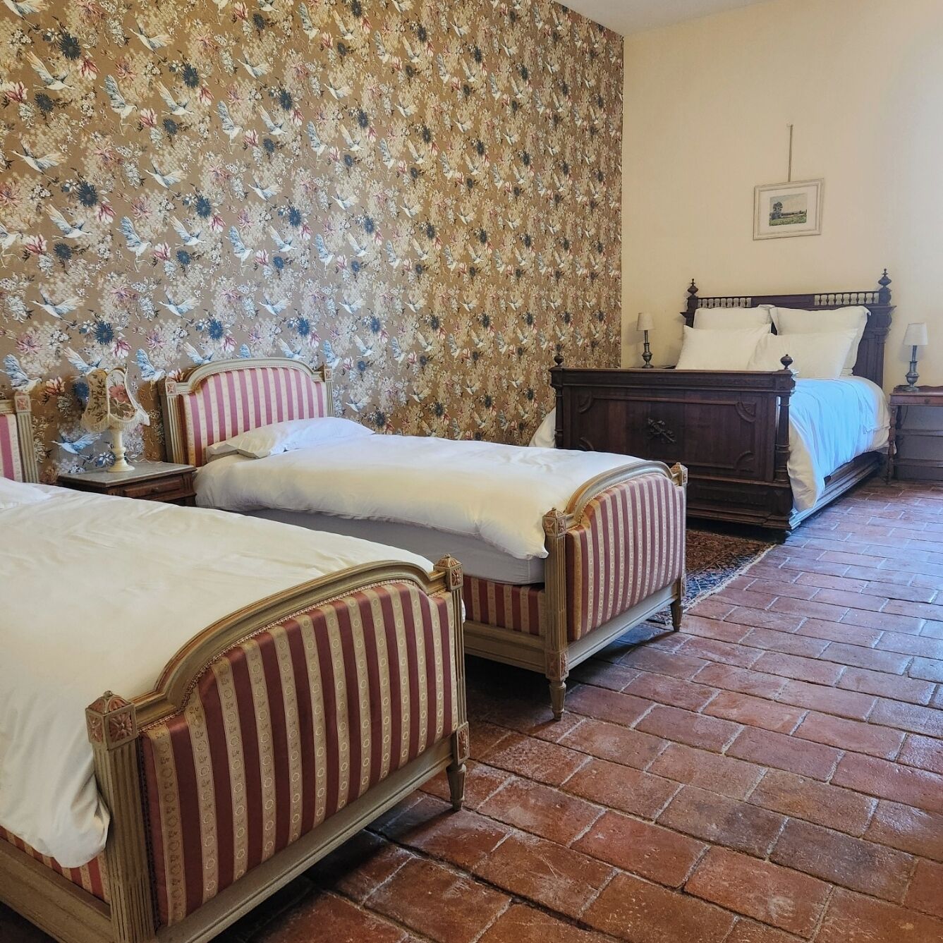 Ein Schlafzimmer mit zwei Betten, einem hölzernen Kopfteil, blumigem Tapetenmuster und einem Backboden.