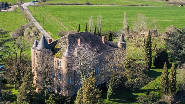 Un château doté de nombreuses tours, entouré d’une pelouse bien entretenue et d’arbres.