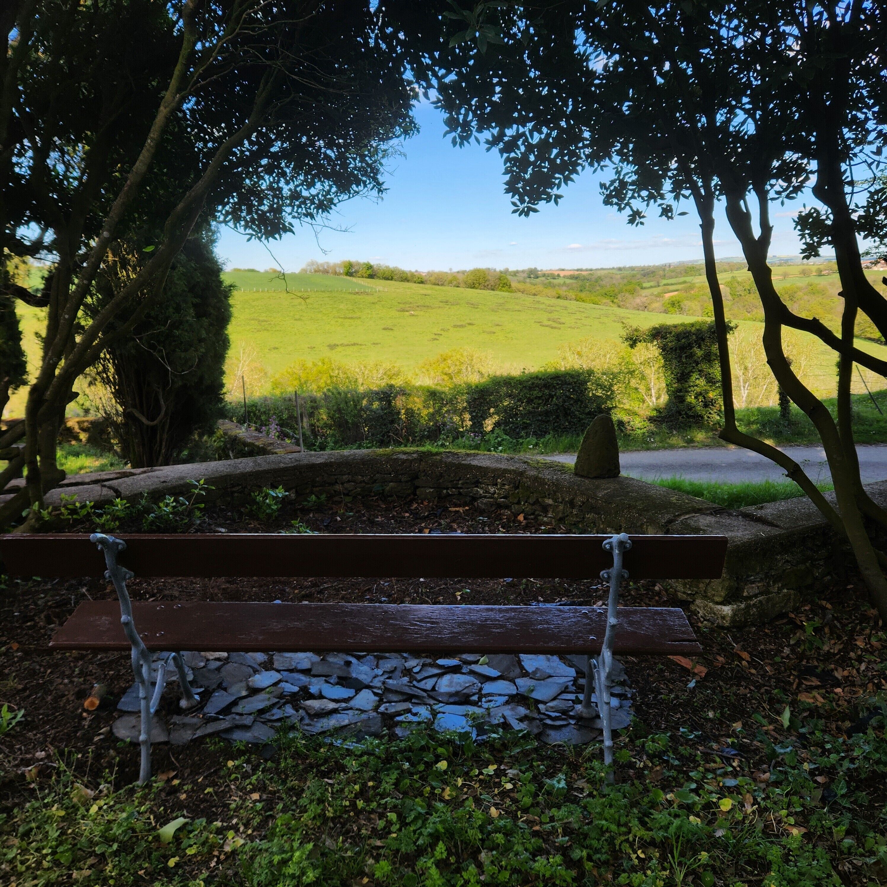 Un banco de piedra en un parque con un muro de piedra y un campo de césped al fondo.