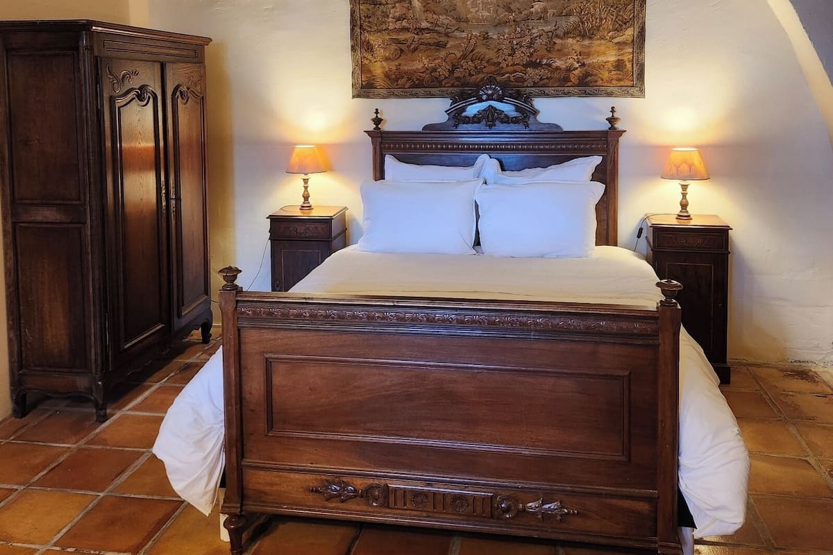 Une chambre à coucher avec un lit en bois, deux tables de chevet avec des lampes, un grand tableau au mur et une armoire.