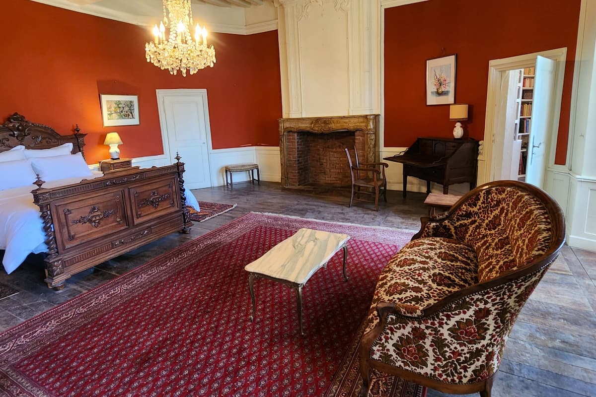 Une pièce comprenant un lit, un lustre, une cheminée, un canapé et un tapis.
