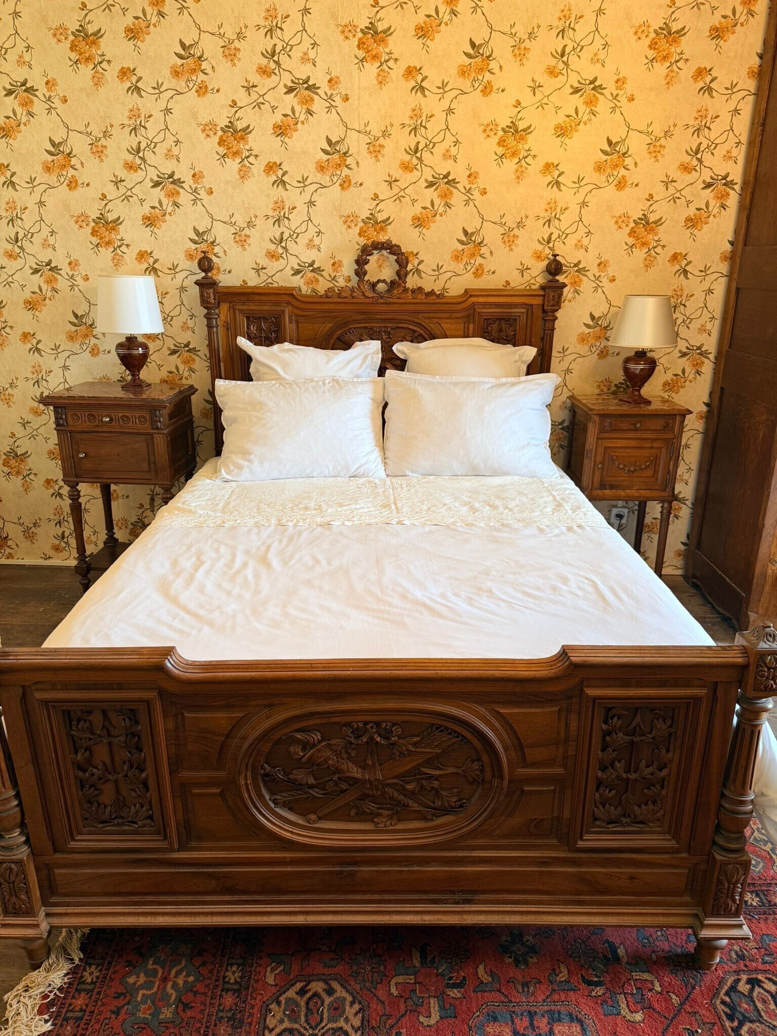 A four-poster bed with a floral wallpaper background and a patterned rug.