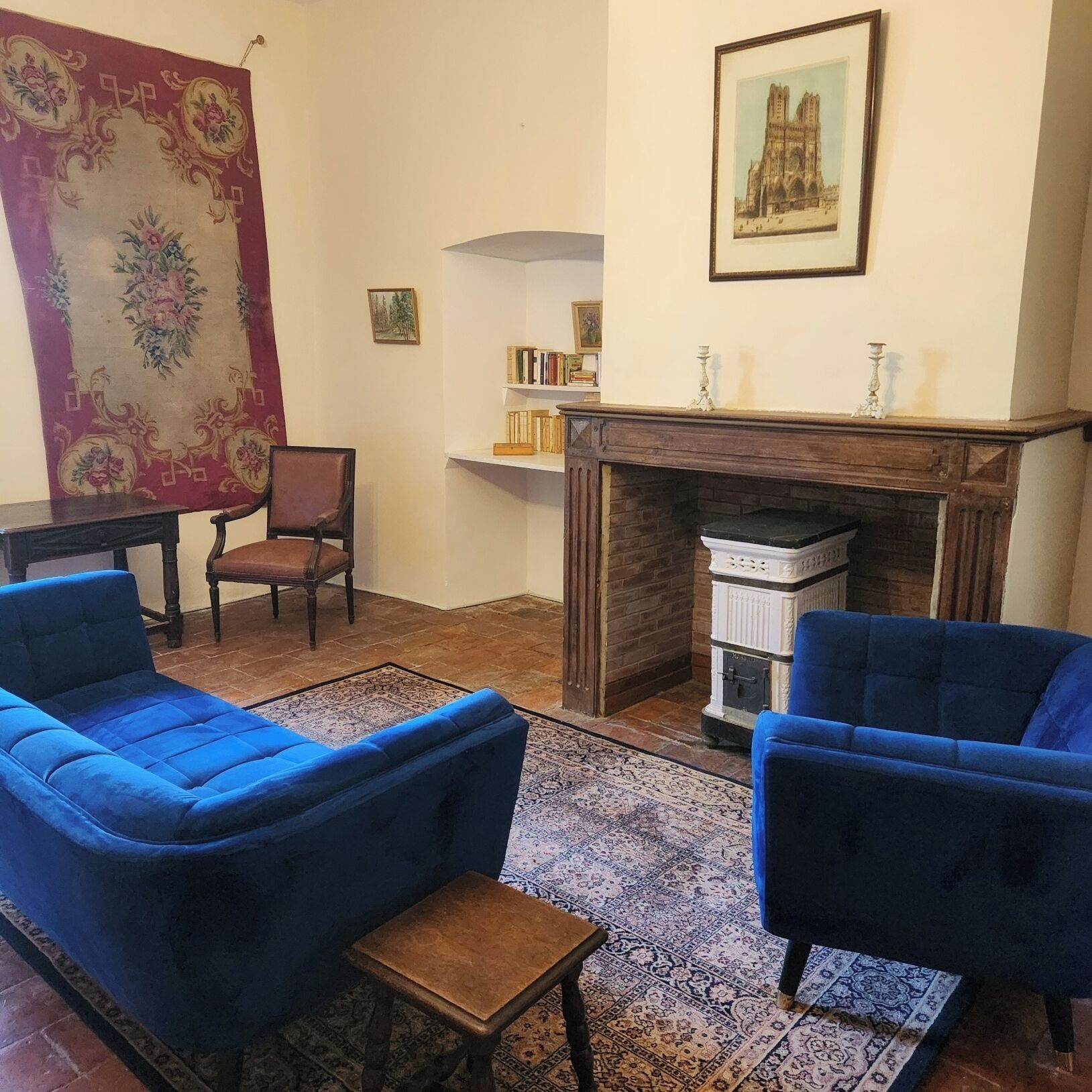 Un salon avec des canapés bleus, une cheminée, un tapis à motifs et une bibliothèque.