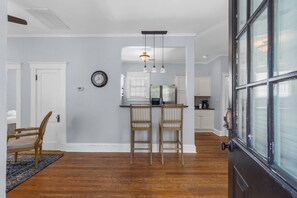 A modern kitchen with white cabinets, a refrigerator, and a dining area with two wooden chairs and a rug. - Upper Carriage House at Wayne Estate (Savannah)