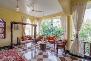 A room with a checkered floor, a canopy bed, a sofa set, a coffee table, and a view of greenery outside. - Alaya Stays Abhimanyu Mansion Pearl (Udaipur)