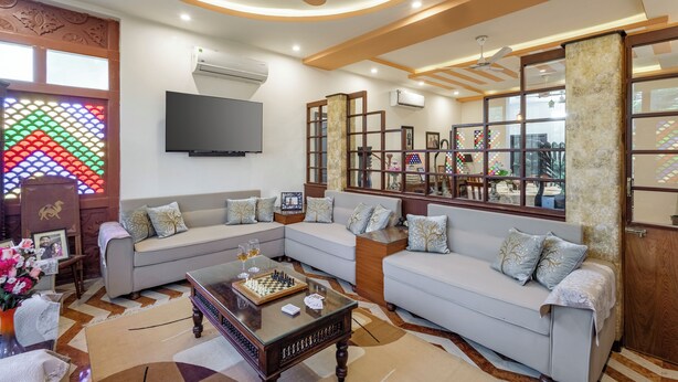 Una sala de estar con un conjunto de sofás, una mesa de centro con ajedrez y vino, un televisor y un ventanal decorativo de vitral.