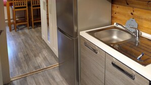 A kitchen with a stainless steel refrigerator, wooden cabinets, a sink, and a dining area with chairs and a table.
