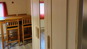 A room with wooden ceiling, white walls, a wooden dining table with chairs, and a white wardrobe with a mirror.