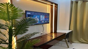 A modern living room with a flat-screen TV mounted on a wall, a wooden coffee table, and a potted plant. - Tranquil studio with AC in enjoyable Greater Noida location (Greater Noida)