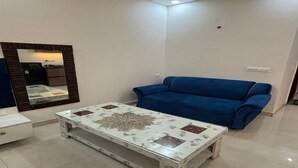 A living room with a blue sofa, a white coffee table with a floral design, and a mirror with a wooden frame. - Tranquil studio with AC in enjoyable Greater Noida location (Greater Noida)