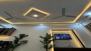 A modern room with a ceiling fan, recessed lighting, a flat-screen TV, and potted plants. - Tranquil studio with AC in enjoyable Greater Noida location (Greater Noida)