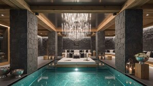 Una habitación lujosa con una piscina grande, paredes de piedra, vigas de madera y un candelabro.