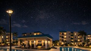 Ein Resort bei Nacht mit Swimmingpool, Liegestühlen und einer überdachten Pavillon.