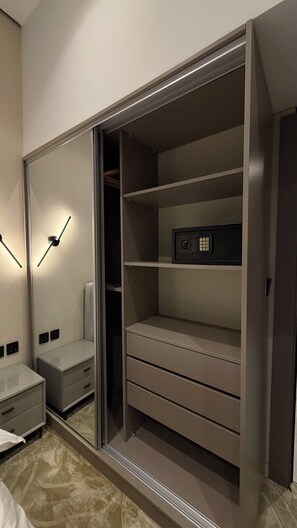 Ein begehbarer Kleiderschrank mit einem Spiegelkorpus, einem Safe und einem Nachttisch.
