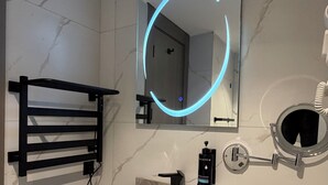 Ein modernes Badezimmer mit Marmorwaschbecken, einem schwarzen Handtuchhalter, einem Spiegel mit blauer Beleuchtung und einem runden Spiegel an der Wand.