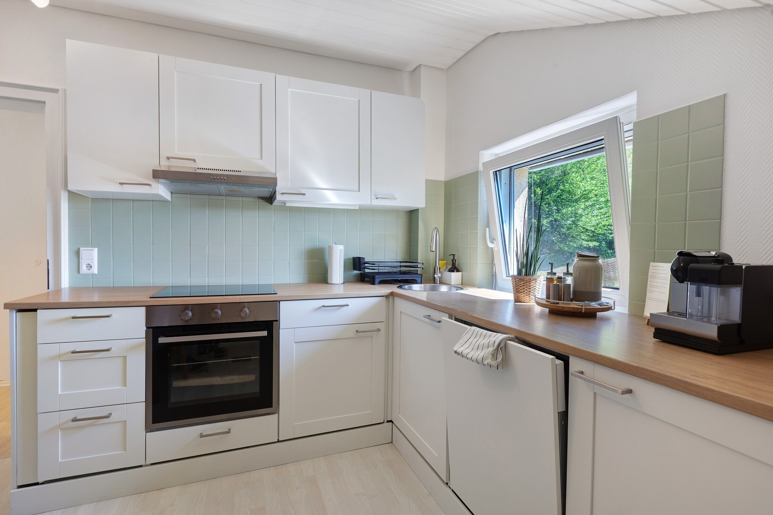 A modern kitchen with white cabinetry, a built-in oven, and a coffee machine.