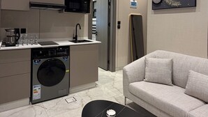 Una cocina moderna con microondas, cafetera y lavadora. Hay un sofá y una mesa baja con un control remoto y una caja.