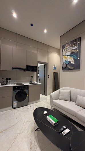 A modern kitchen with a microwave, coffee maker, and a washing machine. There is a sofa and a coffee table with a remote control and a box. - 104 tara-JRE Al Lweibdeh 2BDR with stunning view (Amman)