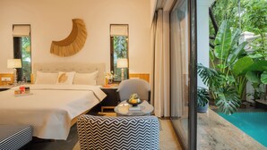 Une chambre avec un lit, des tables de chevet, une chaise, une petite table sur laquelle se trouve un saladier rempli de fruits, et une vue sur une piscine.