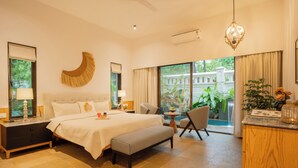 Une chambre spacieuse avec un grand lit, des tables de chevet, un banc, une chaise, une petite table et une vue sur l’extérieur grâce à de grandes fenêtres.