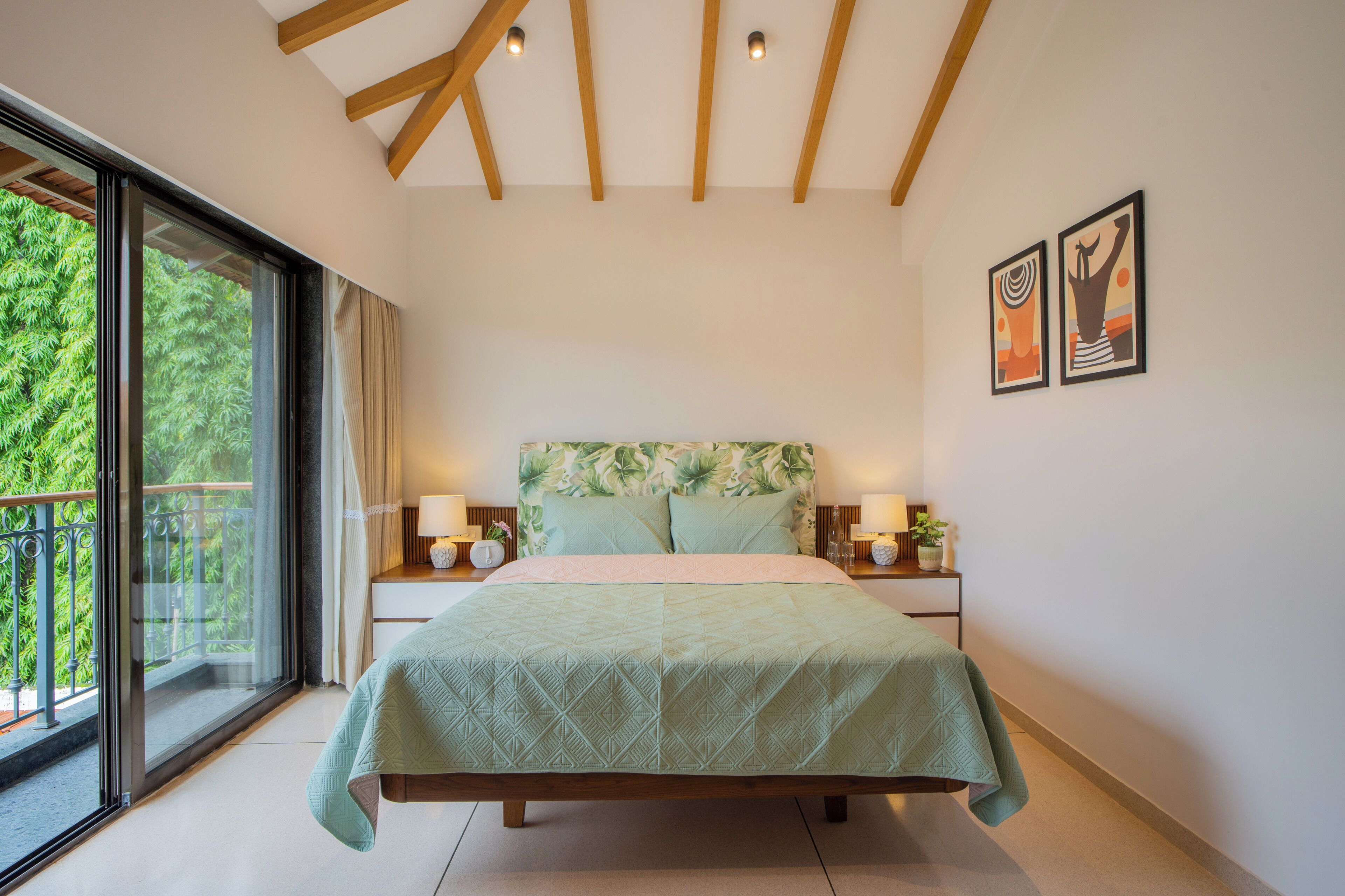 A bedroom with a bed, a window with a view of greenery, a wooden ceiling, and two wall-mounted artworks.