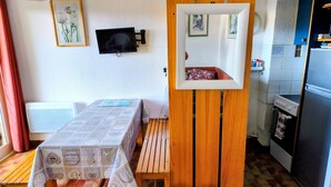 A compact kitchen with a dining area, a wall-mounted TV, and a small refrigerator. - 2-room apartment in residence with swimming pool overlooking Ajaccio bay (Porticcio)