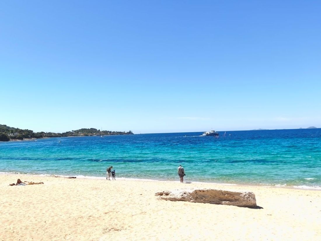 A beach with clear blue water, a sandy shore, and a few people.