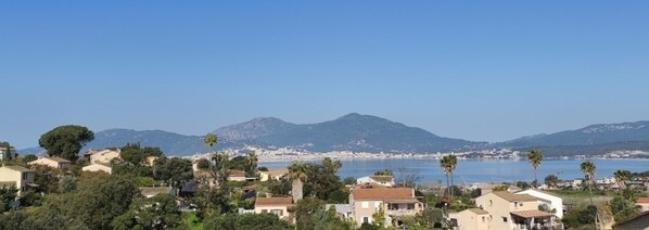 Un pueblo costero con casas, palmeras y montañas al fondo.