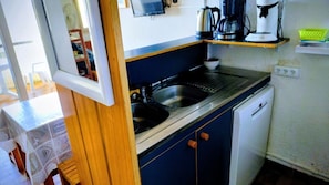 Una cocina compacta con lavamanos, cafetera y lavavajillas.