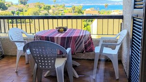 A balcony with a table and chairs, a view of a coastal landscape, and a mountain in the distance. - 2-room apartment in residence with swimming pool overlooking Ajaccio bay (Porticcio)
