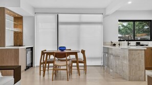 A modern kitchen with a dining area, featuring a large window, a bar area, and a built-in oven. - Spacious North Bondi Apt w Balcony near beach (North Bondi)
