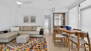 A modern living room with a sofa, a dining table with chairs, and a colorful geometric rug. - Spacious North Bondi Apt w Balcony near beach (North Bondi)