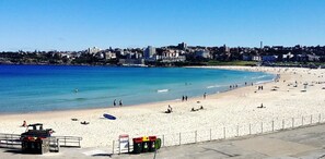 A beach with a lifeguard tower, a recycling station, and a clear view of the ocean and cityscape in the background. - North Bondi Village Living, Walk to Cafés & Dining (North Bondi)