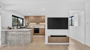 A modern kitchen with a large island, bar stools, a flat-screen TV mounted on the wall, and wooden cabinets. - Spacious North Bondi Apt w Balcony near beach (North Bondi)