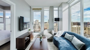 A modern living room with a large window, a sofa, a coffee table, and a TV. - Epic River Valley View | 20th floor | Near Rogers (Edmonton)