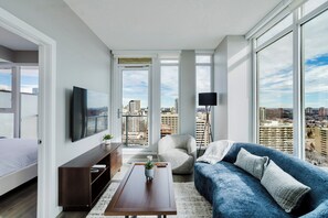 Ein modernes Wohnzimmer mit großem Fenster, einer Couch, einem Couchtisch und einem Fernseher.