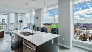 A modern kitchen with a large island, a dining area with chairs, and large windows offering a city view. - Epic River Valley View | 20th floor | Near Rogers (Edmonton)