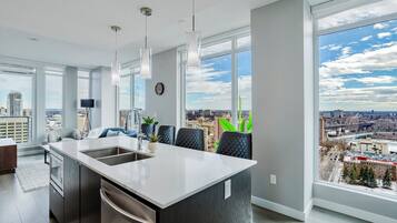 A modern kitchen with a large island, a dining area with chairs, and large windows offering a city view.