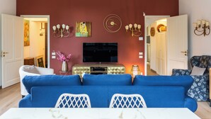 Una sala de estar con un sofá azul, un televisor y una mesa de comedor con cubierta de mármol blanco.
