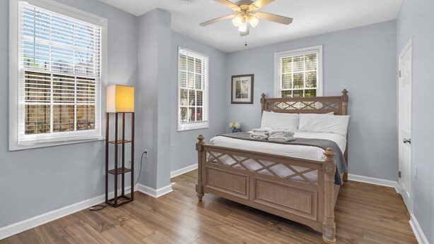 A bedroom with a wooden bed, a standing floor lamp, and a ceiling fan. - Lower Carriage House at Wayne Mansion Estate (Savannah)