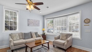 A living room with two sofas, a coffee table, a ceiling fan, and large windows with blinds. - Lower Carriage House at Wayne Mansion Estate (Savannah)
