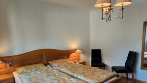Un lit double avec une couvre-lit à motifs floraux, des tables de chevet avec des lampes, une chaise et un plancher en bois.