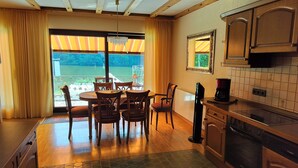 Une cuisine dotée de meubles en bois, d’un four Bosch, d’un coin repas avec une table et des chaises, et offrant une vue dégagée grâce à de grandes fenêtres.