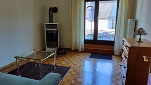 Un salon avec une table basse en verre, un canapé, une cheminée, un plancher en bois et une vue sur l’extérieur, visible à travers une porte vitrée.