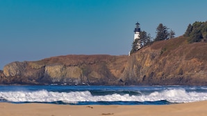 A coastal scene with a lighthouse on a cliff, waves crashing onto the shore, and a clear sky.