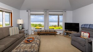 A living room with a sofa, a coffee table, a TV, and a view of the ocean.