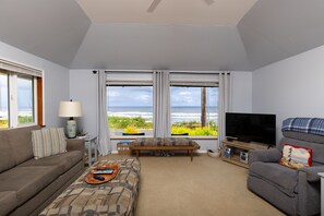 A living room with a sofa, a coffee table, a TV, and a view of the ocean.