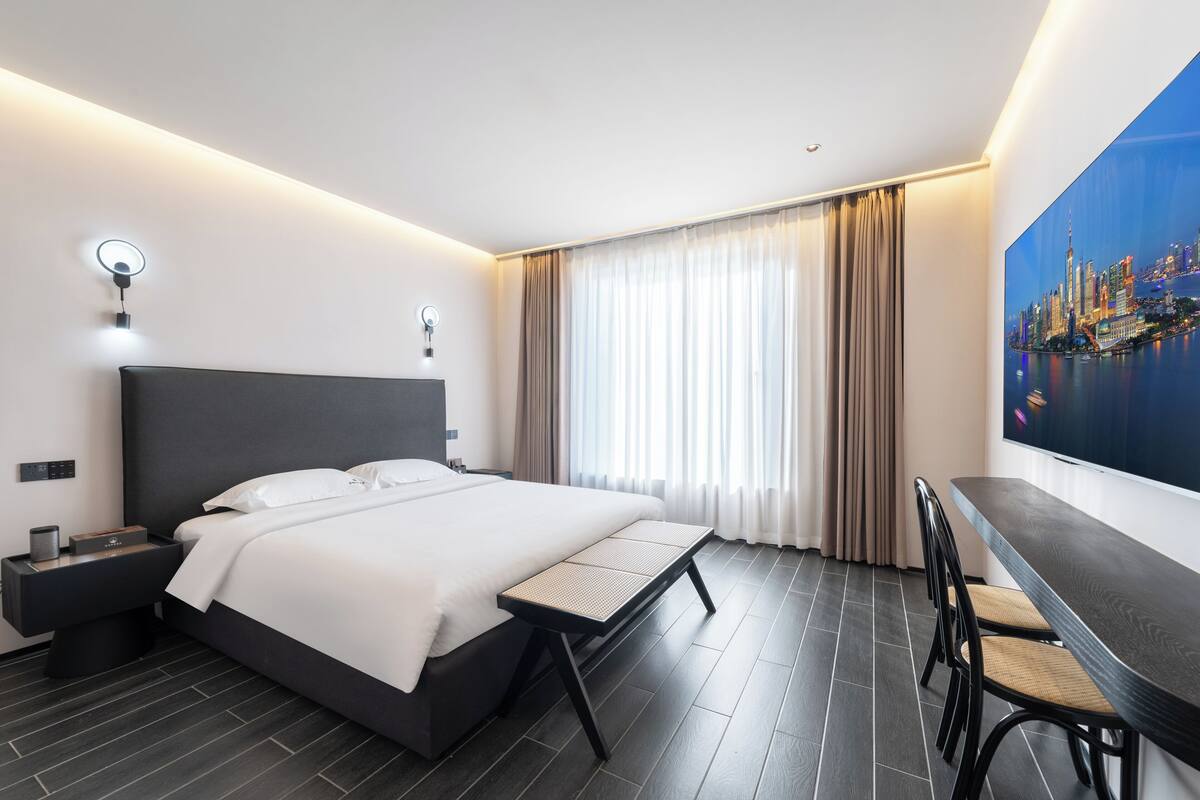 A modern hotel room with a bed, bedside table, lamp, and a cityscape painting on the wall.