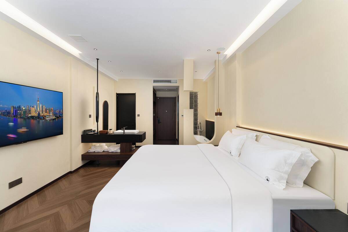 A hotel room with a large bed, a flat-screen TV, a vanity with a mirror, and a door leading to another room.
