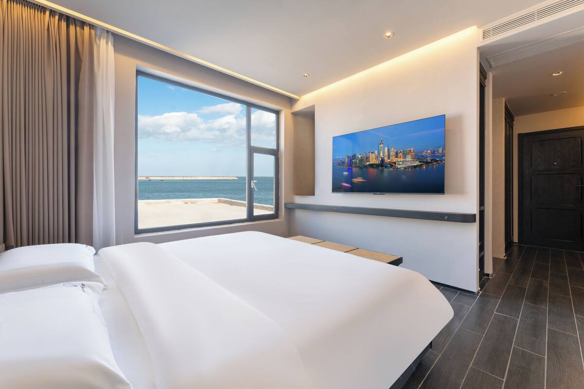 A hotel room with a large bed, a cityscape painting, and a view of the sea.